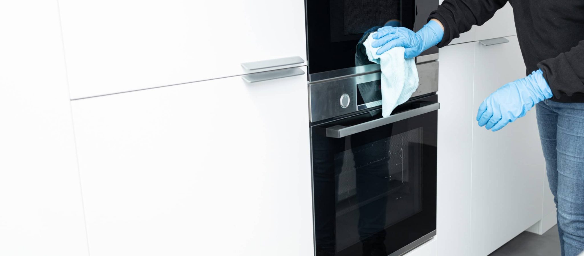 Woman cleaning a modern stainless steel appliances with rag of a minimalist kitchen